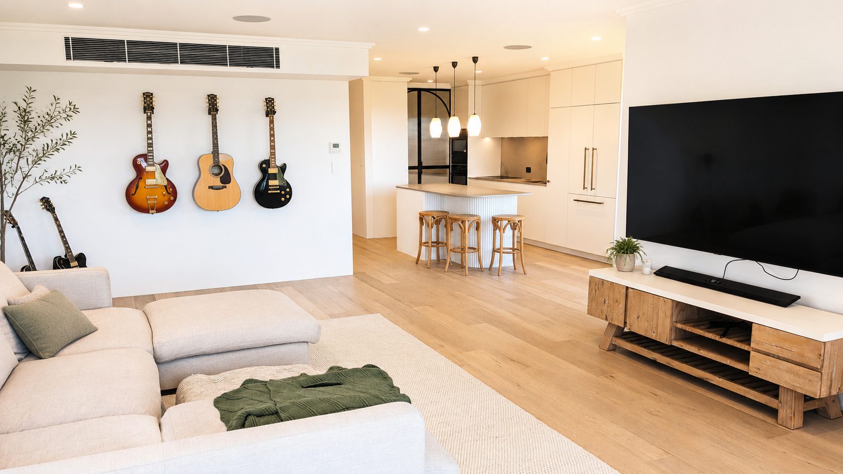Renovated open-plan living area and kitchen in Cronulla by Armessen Build, with timber flooring, white cabinetry and guitars on the wall